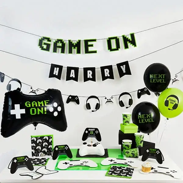 Gaming-themed party setup with game controller decorations, Game On banner, balloons, and coordinated tableware in black and neon green